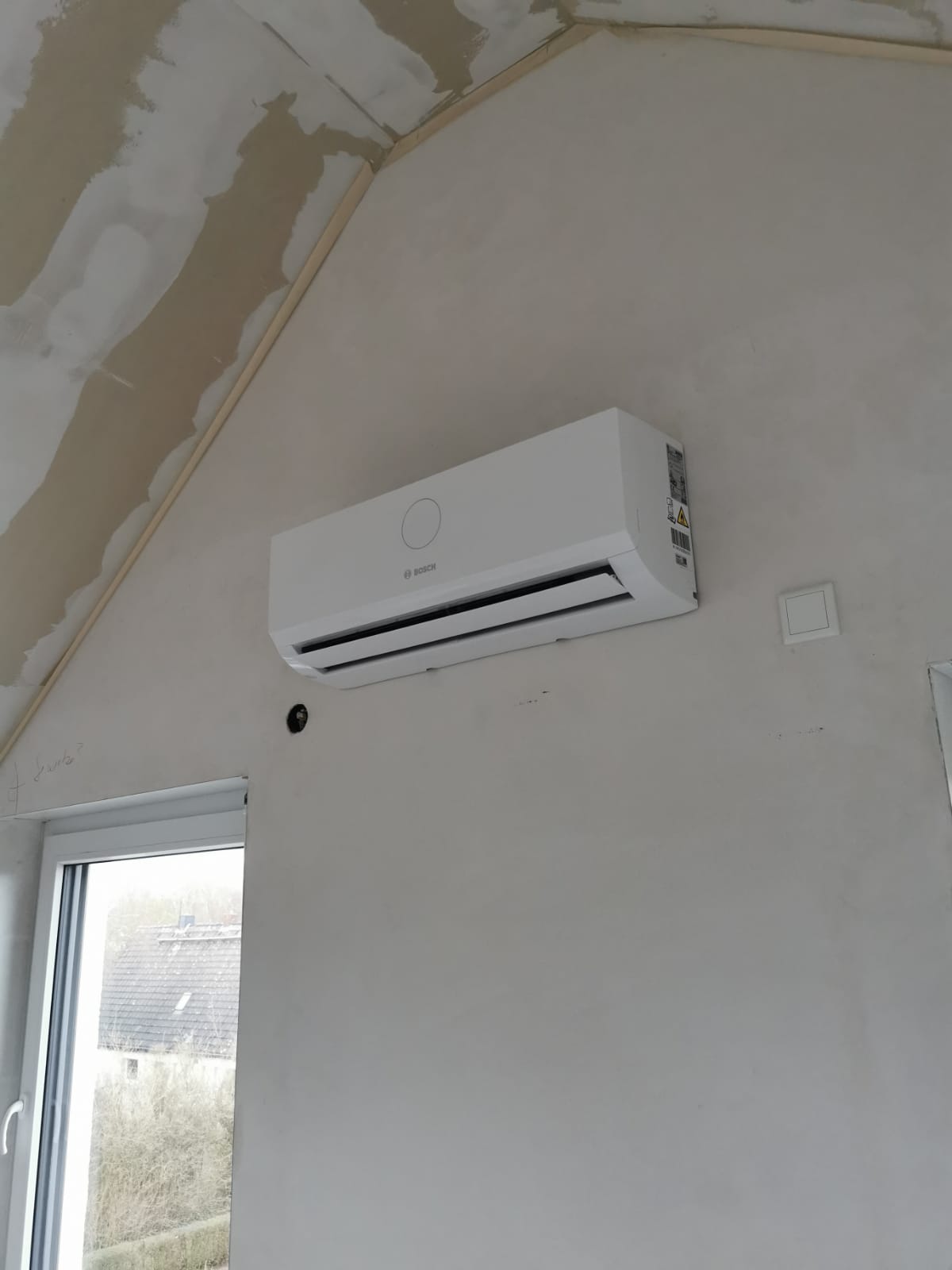 Wandmontiertes Innengerät einer Bosch-Klimaanlage, dezent oberhalb eines Fensters installiert, bereit zur Raumkühlung oder -heizung.
